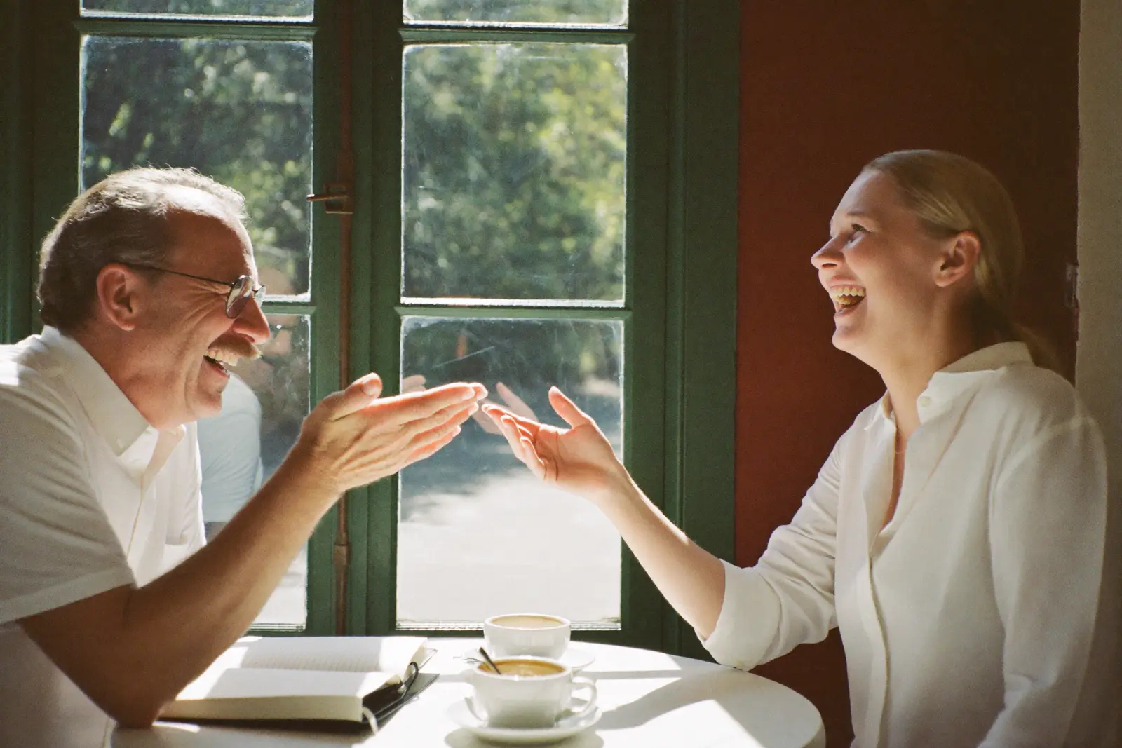 Zwei Menschen lachen miteinander bei Kaffee am Fenster